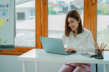 Attractive young Asian beauty accountant in office using laptop and financial documents on office desk.