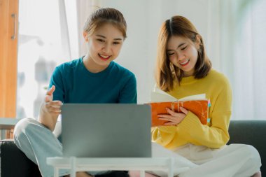 Two Asian women use their laptop computers on the couch to surf the Internet to shop online safely while at home.