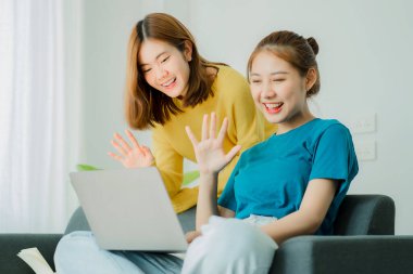Two Asian women use their laptop computers on the couch to surf the Internet to shop online safely while at home.