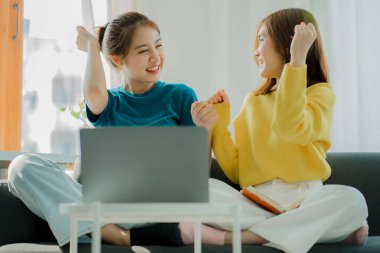 Two Asian women use their laptop computers on the couch to surf the Internet to shop online safely while at home.