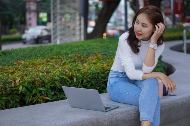 Asian young woman or young student sitting with laptop outdoors, online learning concept.