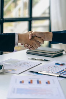Young businessmen shake hands after a short job to sign a co-working business contract in a modern office with vintage-style images of colleagues at a teamwork meeting.