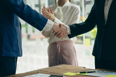 Young businessmen shake hands after a short job to sign a co-working business contract in a modern office with vintage-style images of colleagues at a teamwork meeting.