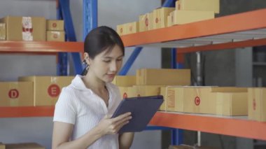 Beautiful Asian woman preparing orders for customers. and answer the customer on the laptop computer at her shop at home. Online business influencers on social media, packaging and shipping ideas.