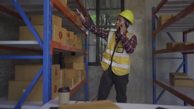 Young manager checking stock on clipboard in warehouse Side view of young Asian warehouse worker with helmet checking order details with digital tablet at inventory room.