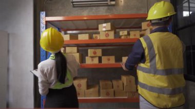 Male and female warehouse workers prepare goods for transportation.Ready stock check on clipboard in warehouse. Side view of young Asian warehouse worker with helmet checking order details