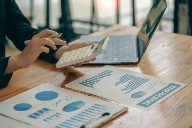 An accountant presses a calculator, calculates finances, analyzes graphs, reports finances at a desk in the office.