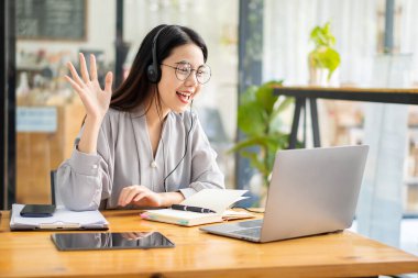 Pretty Asian woman and headphones using laptop in coffee shop writing notes. Attractive female student learning language. View webinars online. audio course education