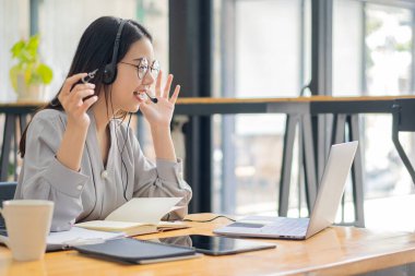 Pretty Asian woman and headphones using laptop in coffee shop writing notes. Attractive female student learning language. View webinars online. audio course education