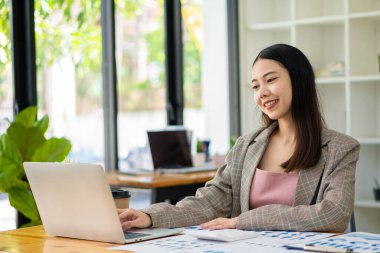 Asian businesswoman working on laptop and documents at the office Doing financial math on a wooden table in the office. Taxes. Accounting. Financial concepts.