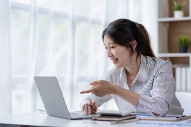 Asian woman working at home on desk using calculator to calculate tax accounting expense report with graph document and laptop computer.