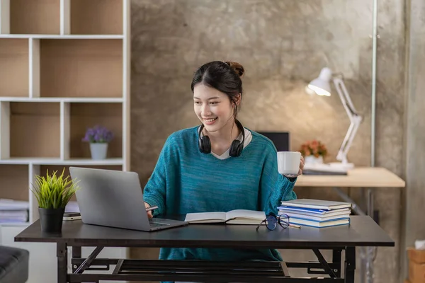 Smiling Asian woman using headset looking at laptop screen listen and learn online courses with a video call with headphones for online learning