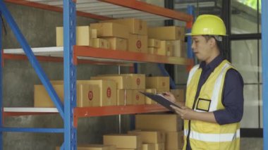 Handsome Asian employee works at a warehouse. Workers wearing high visibility clothes and helmets are checking and counting goods or boxes for delivery. Sme business idea.