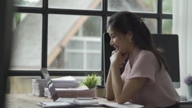 online business Asian female accountant working from home using laptop in meeting with smartphone, financial graphing calculator.