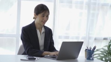 online business Asian female accountant working from home using laptop in meeting with smartphone, financial graphing calculator.