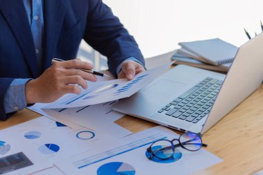 Close-up business concept of accountant holding graph document working on calculator to calculate financial data report Accounting documents and laptop computer at the office, close-up