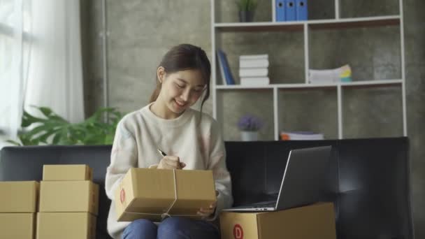 自宅でソファに座っているアジアの女性は ボックスやラップトップで顧客からの注文を受けてオンラインビジネスいくつかの販売コンセプト — ストック動画