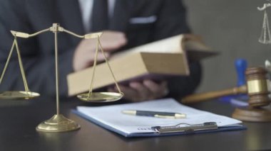 Avukatlar ofiste hukuk kitapları okurlar. Görüntülerde bir Adalet Anıtı modeli, ahlaki gücün kişileştirilmesi yer alıyor. Hakimin çekici de masanın üstünde.