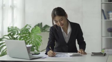 Ev geliri ve gider bütçe planlayıcısının grafikleri için hesap makinesiyle hesap makinesi kullanan Asyalı bir iş kadını. Bilgisayarlı çevrimiçi toplantılarla finansman