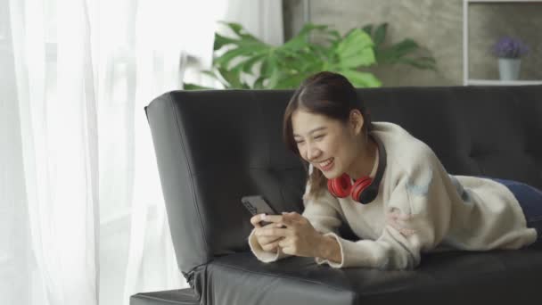 Linda Mujer Asiática Sentada Sofá Jugando Juego Con Teléfono Inteligente — Vídeos de Stock