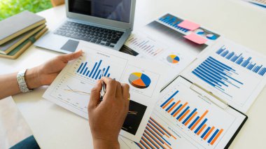 Şirketin mali verilerini gösteren kalem ve pasta çizelgesi tutan işadamı dizüstü bilgisayarlı özel bir ofiste oturup finansal verileri harita halinde analiz ediyor. finansal kavram