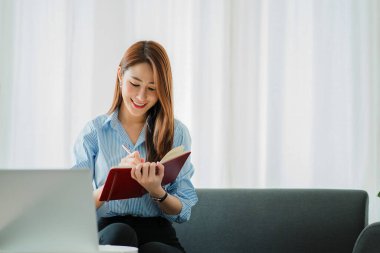 Evde dizüstü bilgisayarla çalışan Asyalı bir kadın kanepeye oturmuş online çalışma konsepti geliştiriyor.
