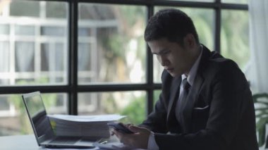 Genç Asyalı işadamı, defter, bütçe, vergi, finansal dökümanlar kullanırken gelir ve ev harcamalarını kaydediyor. Ev ekonomisi konsepti 4k 'de oturma odasında çalışmak.