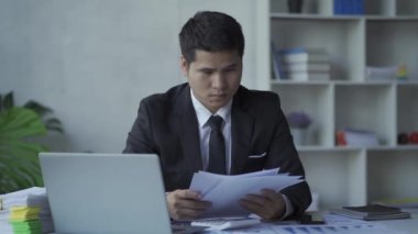 Genç Asyalı işadamı, defter, bütçe, vergi, finansal dökümanlar kullanırken gelir ve ev harcamalarını kaydediyor. Ev ekonomisi konsepti 4k 'de oturma odasında çalışmak.