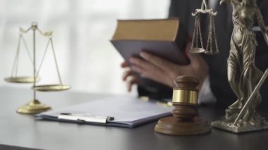Masasında elinde çekiçle hukuk kitabı okuyan bir avukat ve Avukat Kok 'un demek istediği adalet tanrıçası..