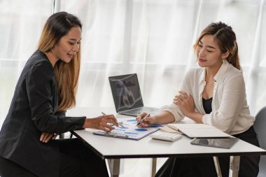 Bir grup Asyalı iş kadını bir şey tartışıyor ve birlikte çalışan kadınların ofisindeki bir masada oturup mali durumu analiz ederken gülümsüyorlar..