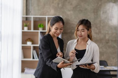 İki güzel Asyalı kadın online alışveriş için ekranlara bakan tabletler kullanarak ortak bir yapıya danışıyorlar. İnternet işbirliği kavramı