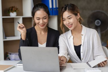 İki güzel Asyalı kadın, çevrimiçi iş için ekranlara bakan dizüstü bilgisayarları kullanarak birlikte çalışmanın yapısını tartışıyor. İnternet işbirliği kavramı