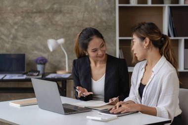 İki güzel Asyalı kadın, çevrimiçi iş için ekranlara bakan dizüstü bilgisayarları kullanarak birlikte çalışmanın yapısını tartışıyor. İnternet işbirliği kavramı