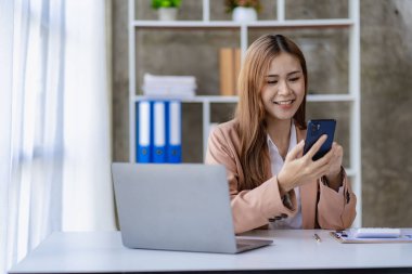 Muhasebe Finans 'ta çalışan Asyalı genç iş kadını. Akıllı telefonlar ve bilgisayarlarla bürodaki masanın üstünde evraklar var..