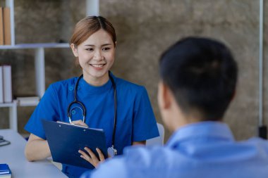 Asyalı kadın doktor, klinikte tekerlekli sandalyedeki erkek hastaya tavsiye ve teşvik veriyor.