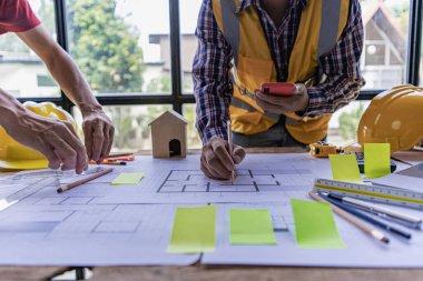 Ofiste çalışan mühendis bir inşaat projesi çiziyor. Bir mimarın el yazısı mühendisi, modern bir ofisteki bir masada mimari planlar üzerinde kat planlarını tartışıyor..