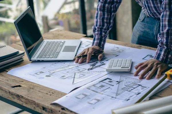 engineer working in office draw a construction project An architect\'s hand-drawn print engineer discusses floor plans over architectural blueprints at a desk in a modern office.