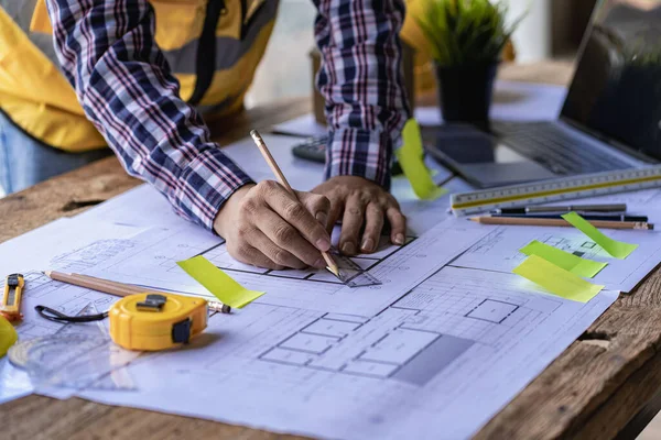 engineer working in office draw a construction project An architect\'s hand-drawn print engineer discusses floor plans over architectural blueprints at a desk in a modern office.