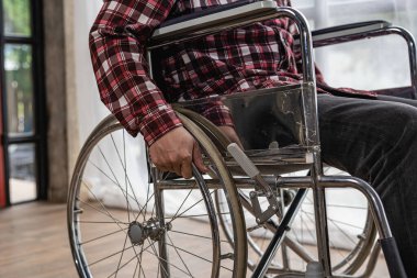 Kırmızı kareli gömlekli yüzünü göremeyen bir adam evdeki tekerlekli sandalyede oturuyor..