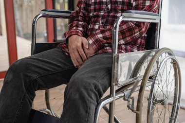 Kırmızı kareli gömlekli yüzünü göremeyen bir adam evdeki tekerlekli sandalyede oturuyor..