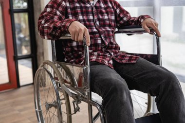 Kırmızı kareli gömlekli yüzünü göremeyen bir adam evdeki tekerlekli sandalyede oturuyor..