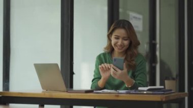 Güzel Asyalı kadın bir kafede akıllı telefon ve dizüstü bilgisayarla çalışıyor ve konuşuyor. çevrimiçi iş kavramı