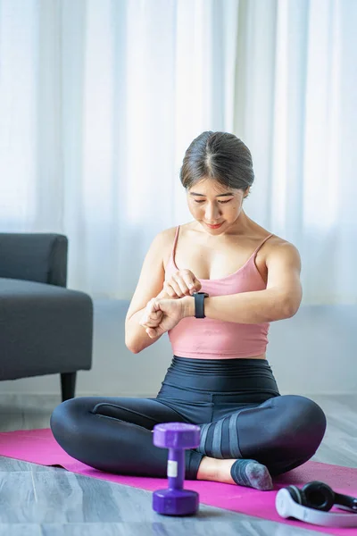Asian woman in sportswear sitting relaxing and practicing yoga and exercising with dumbbells and laptop computer in bedroom at home fitness concept