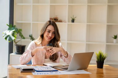 Ofiste çalışan gülümseyen iş kadını elinde para şeması belgesi ve elinde dizüstü bilgisayarla ofis muhasebe konseptinde koltukta oturuyor.