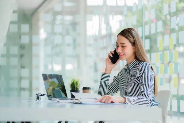 Asian businesswoman in a formal suit in the office is happy and cheerful while using a smartphone to work, financial accounting, analytical concept.