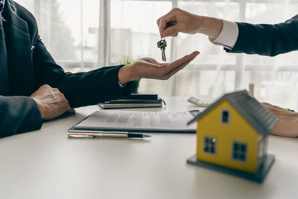 Real estate agents and sales representatives hand out keys from new homes to office clients with examples of homes laid out in front.