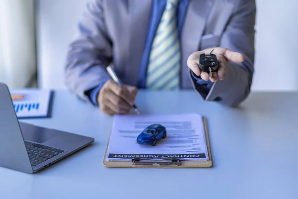 Car sales concept, sales reps give keys to customers on table with small car samples and office insurance.