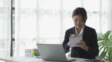 Laptop bilgisayarında çalışan Asyalı iş kadını, gelir bilgisi için grafikleri ve grafikleri ev içi yatırım fikirlerinde kağıt üzerinde görüyor..