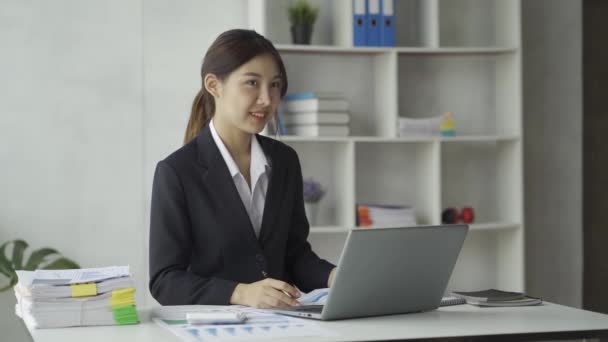 在笔记本电脑上工作的亚洲女商人以及在总部投资理念的纸张上查看图表以获取利润收入信息 — 图库视频影像