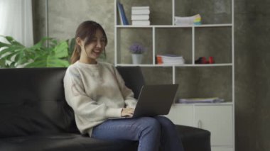 Evdeki kanepede dizüstü bilgisayarla çalışan çekici Asyalı kadın.